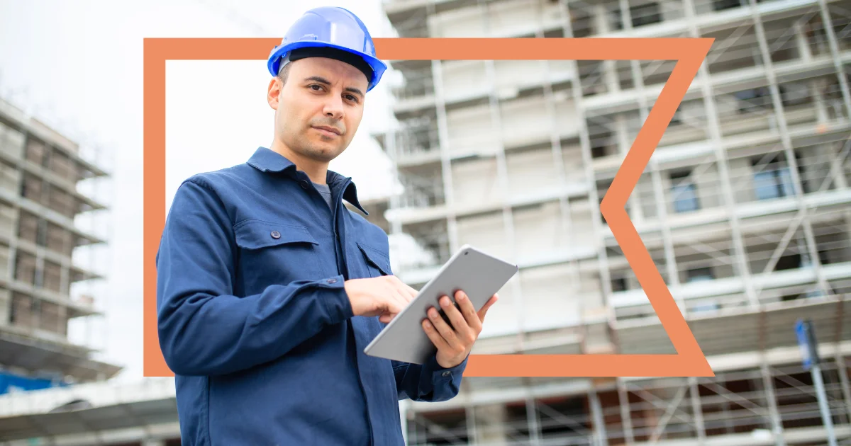 Man in blue hardhat and coveralls holding a tablet with the orange Coastal flag behind him