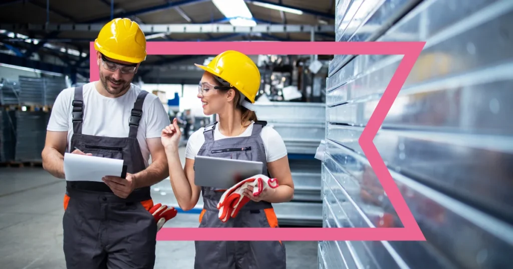 Two industrial workers wearing yellow hard hats and overalls are standing in a warehouse, discussing something. One is holding a clipboard, and the other is holding a tablet, with a pink graphic frame highlighting the scene.