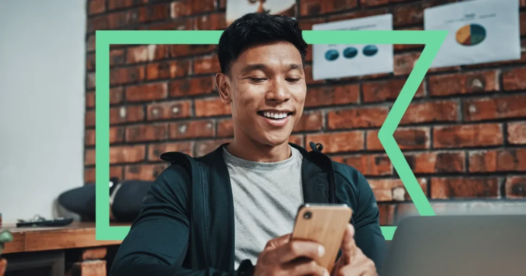 Smiling man using a cell phone in front of a computer